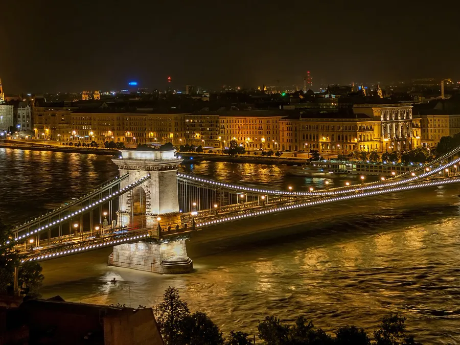 The Széchenyi Chain Bridge lit up at night over the Danube, with the Hungarian Parliament glowing behind