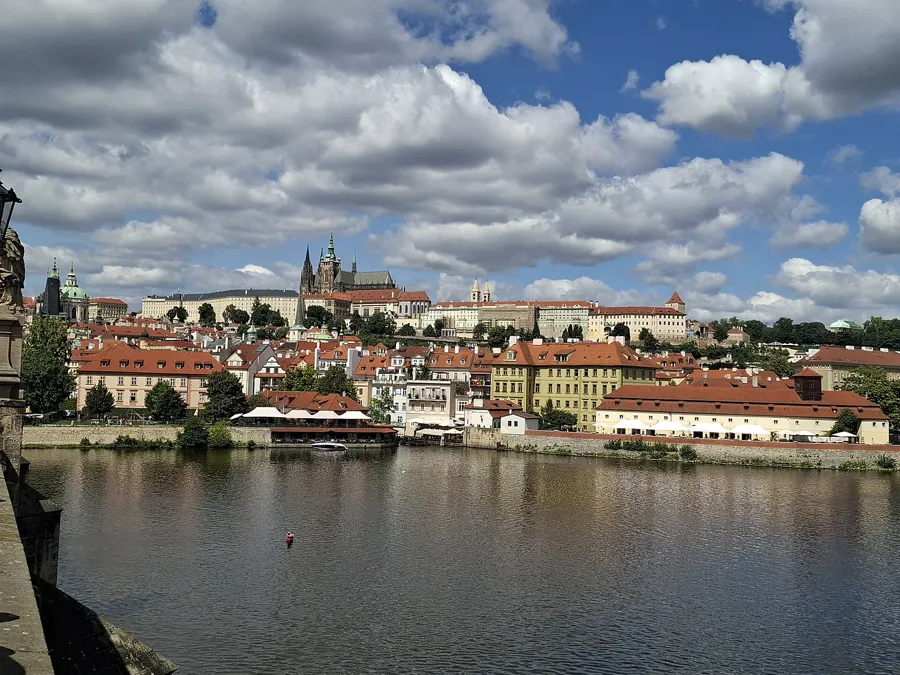 Prague Castle and St. Vitus Cathedral above red rooftops, seen across the Vltava from Charles Bridge